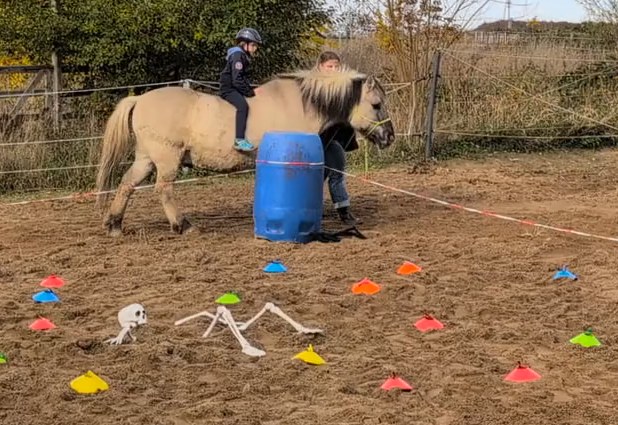 Kind reitet auf dem Pony über den Sandplatz mit Grusel-Deko